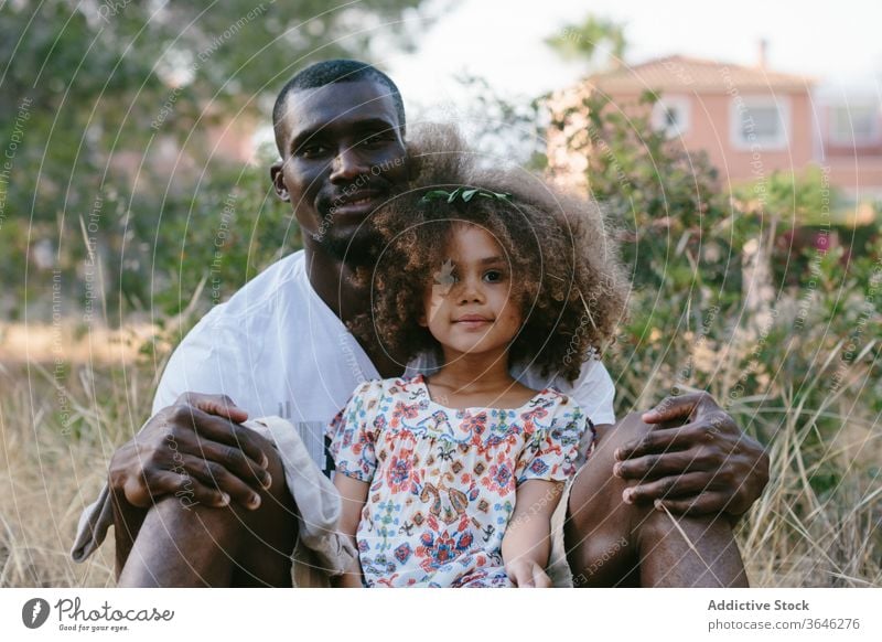 Cheerful black father resting with cute daughter in nature hug meadow countryside adorable summer happy cheerful sit positive casual outfit curly hair girl