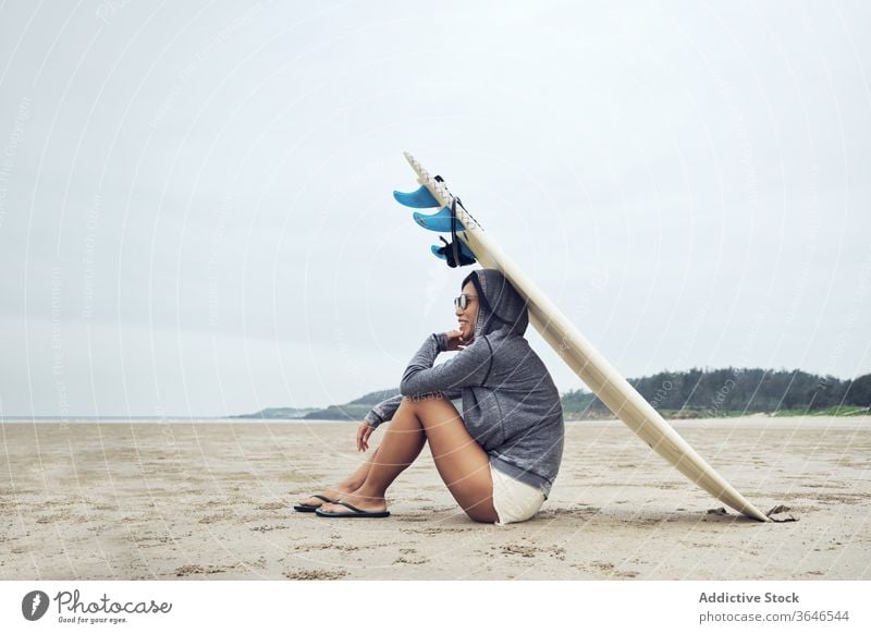 Relaxed woman sitting on beach with surfboard on head surfer rest casual sand relax sporty tranquil sunglasses lifestyle nature seashore seaside weekend ocean