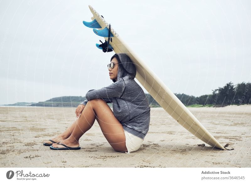 Relaxed woman sitting on beach with surfboard on head surfer rest casual sand relax sporty tranquil sunglasses lifestyle nature seashore seaside weekend ocean