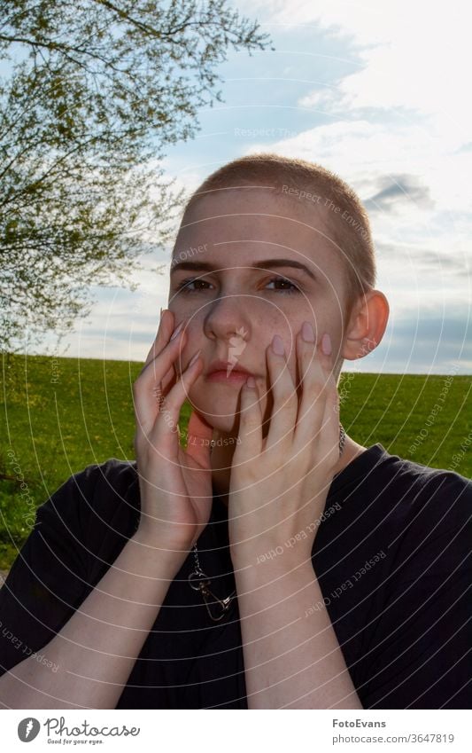 Young woman with very short hair, hands on face, stands in nature portrait sick medicine fashion day beauty nails cancer female attractive girl therapy real