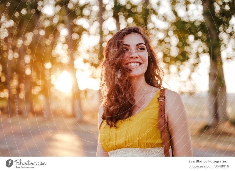 portrait of young beautiful woman wearing a yellow dress walking by a path of trees. Summertime and lifestyle adventure back beauty bright brunette casual