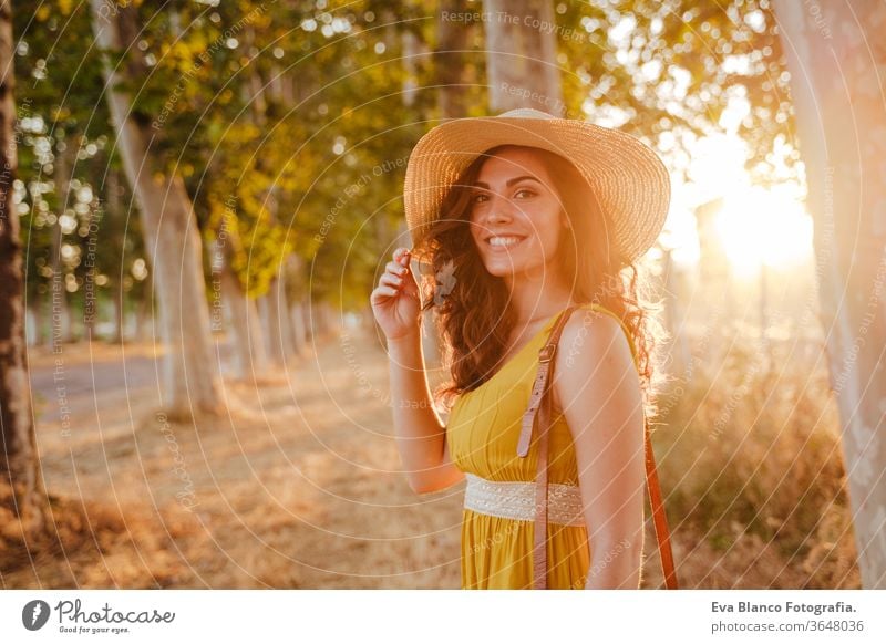 portrait of young beautiful woman wearing a yellow dress walking by a path of trees. Summertime and lifestyle adventure back beauty bright brunette casual