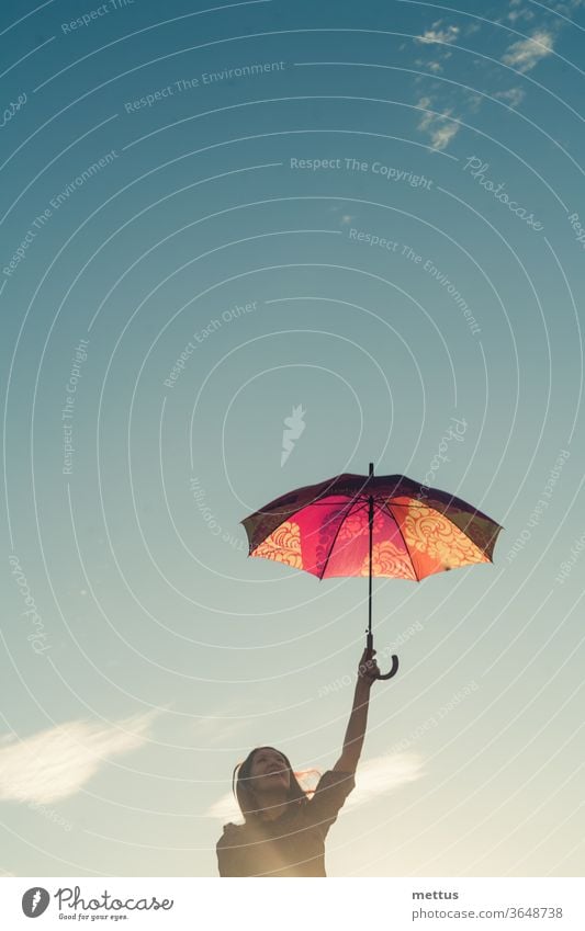 Jolly girl holding colorful umbrella in her hands in front of the sky with space clouds, a lot of copyspace female freedom happy dress emotion classic person