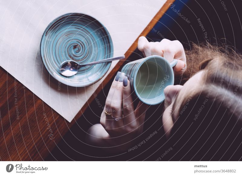 A view from above of a girl drinking tea from a small cup. above view hot drink nostalgia person female sitting top of head loneliness portrait express indoor