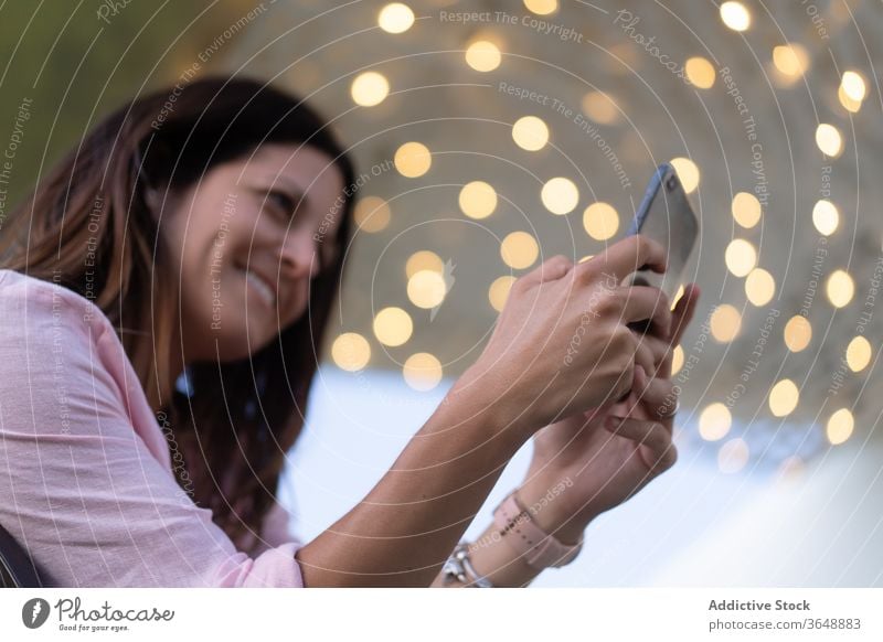 Smiling woman using smartphone outside take photo content illuminate garland memory moment female camera mobile gadget photography cellphone device smile