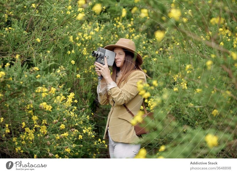 Cheerful photographer walking in park with vintage video camera retro bush bloom flower countryside summer shrub stroll garden nature idyllic calm positive