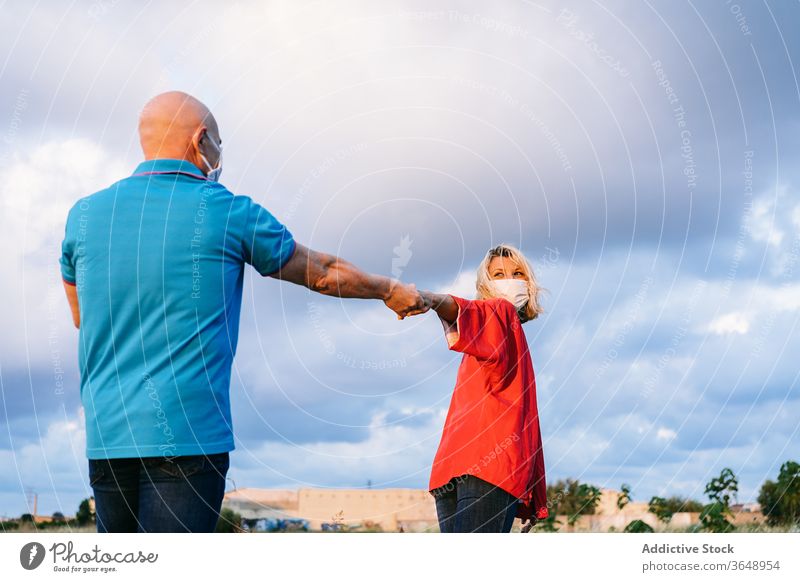 Couple in face masks holding hands and spinning in countryside couple casual summer romantic covid 19 love walk enjoy middle age evening affection content