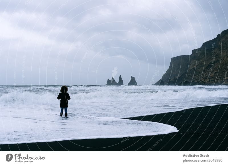 Unrecognizable traveler on beach on cloudy day seascape water cold season seashore rocky landscape wave foam nature vacation tourist adventure holiday coast