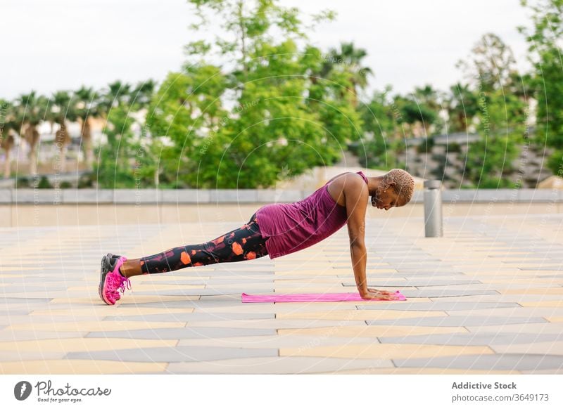 Fit African American woman standing in One Legged Plank pose practice yoga one legged plank pose energy balance endurance concentrate sportswear pavement asana