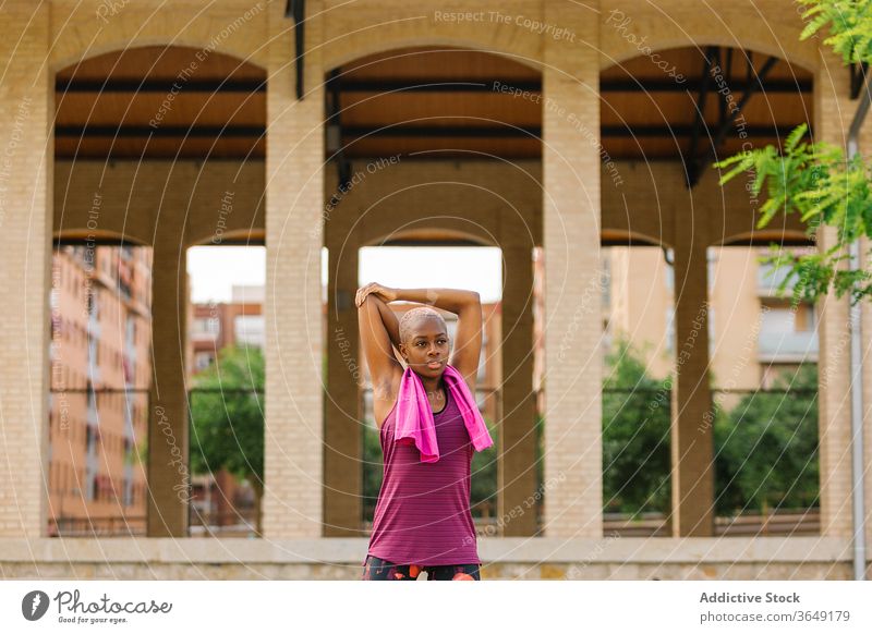 Tired black sportswoman with towel standing on embankment after workout break activewear mouth opened tired healthy building pavement city relax wellness fit