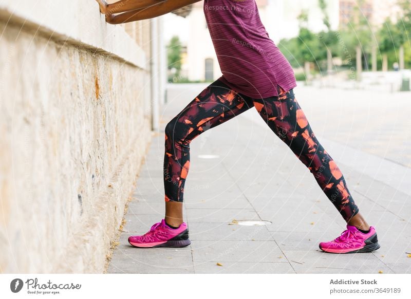 Black sportswoman stretching legs on sidewalk near brick house exercise practice activity sportswear building city healthy column athlete workout training