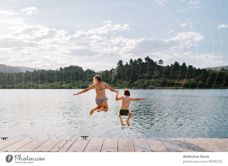 Delighted siblings jumping in lake from pier children having fun water group moment pond childhood swimwear quay wooden weekend summer vacation kid relax joy