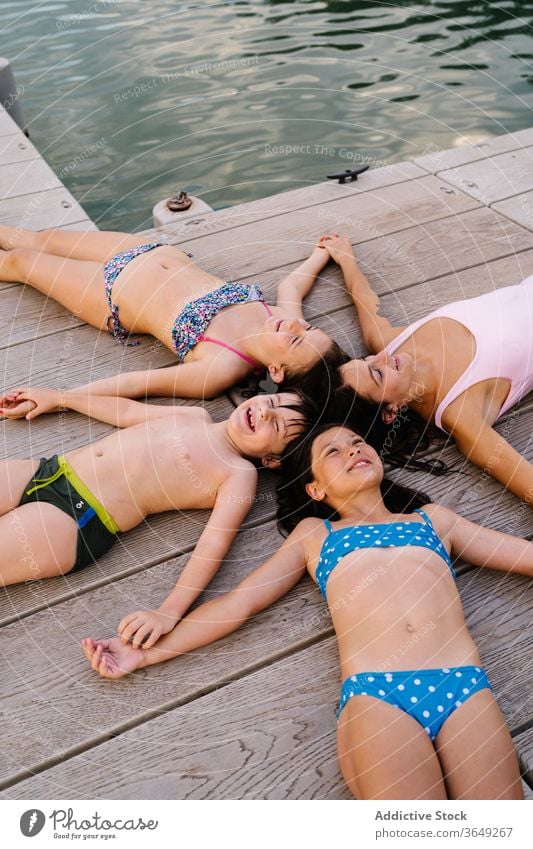 Happy siblings and mother lying on quay children vacation summer pier relax star shape swimwear content rest happy holding hands together unity holiday