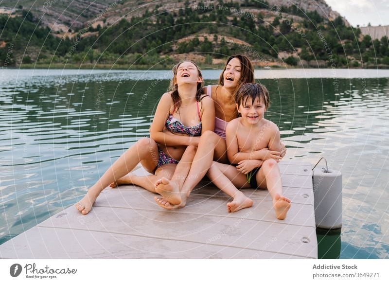 Happy siblings and mother sitting on quay children vacation summer pier relax swimwear content rest happy embrace together unity holiday recreation weekend