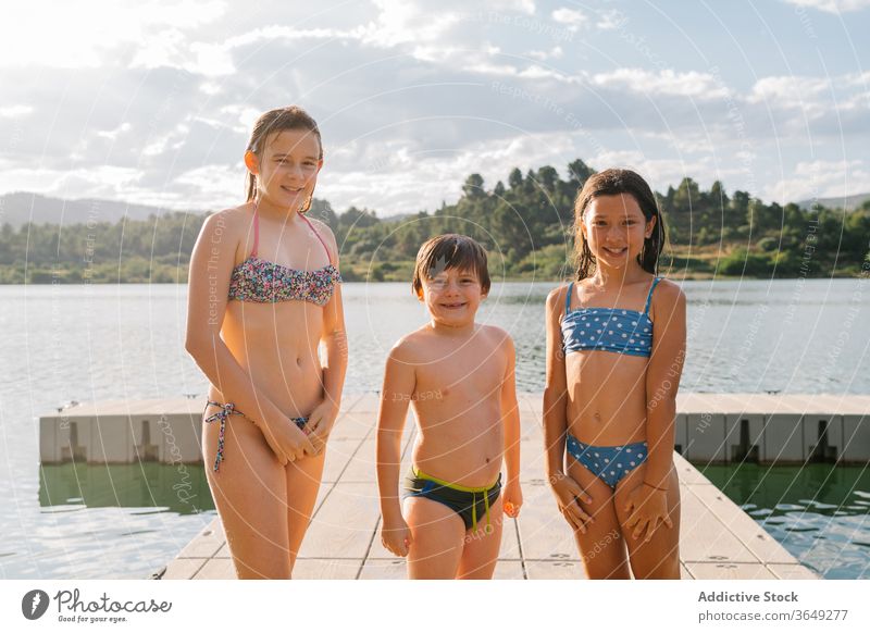 Group of cheerful siblings on wooden pier lake children summer vacation together group swimwear quay brother sister unity friendly friendship happy water rest