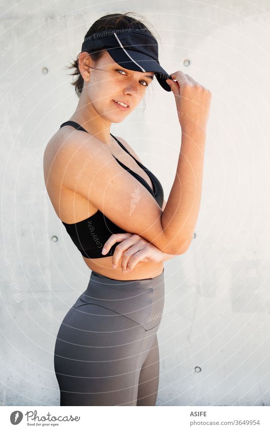 Portrait of a young stylish and beautiful sporty woman posing in the street model fashion portrait running isolated happy smiling runner wall visor cap athlete