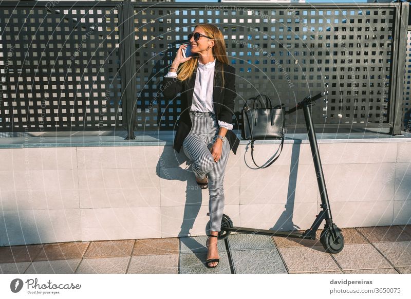 Businesswoman with mobile and her scooter next fashion happy businesswoman e-scooter stylish urban cell phone wall street talking sitting commuter elegant