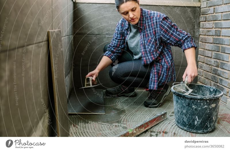 Female mason laying tiles on a terrace woman workman taking cement concrete bucket cube tiling floor imitation cement tile tiler glazed terrace working