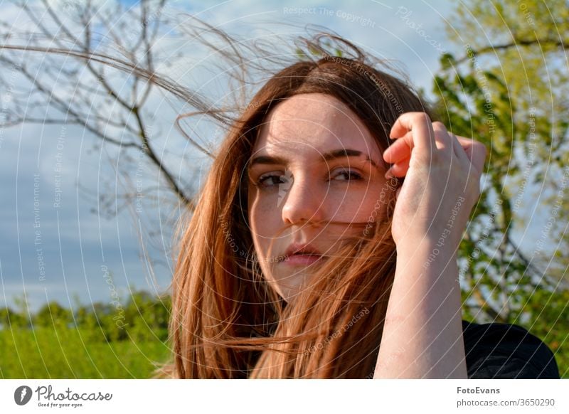 Girl is standing with blowing hair in  nature, hand on head arm wind portrait fashion day beauty modern attractive girl tree outdoors sunlight real person