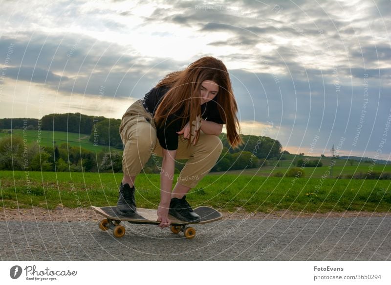 A  girl skates on a road in nature workout sporty enjoying fashion day beauty skating hand modern attractive real fit hobby real person asphalt hair crouching