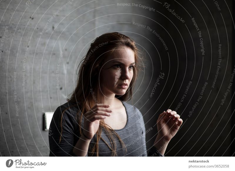 Young Woman Raising Arms Behind Grey Concrete Wall female one person girl portrait hairstyle young woman caucasian ethnicity youth culture concrete brunette