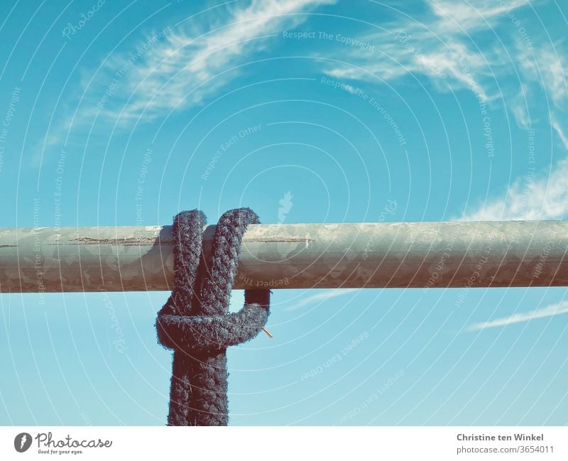 A dark rope tied to a horizontal metal rod. Close-up with blue sky and clouds Rope Dew Knot Metal post String Blue sky little cloud Sky Riding stable paddock