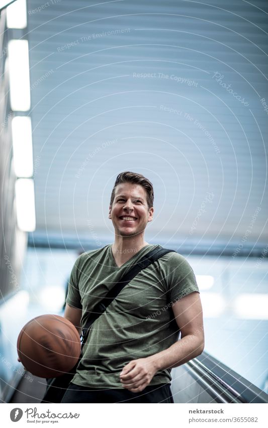 Man Walking Holding Basketball Smiling on Escalator stairwell subway station adult caucasian urban handsome model sport building interior public area urban area