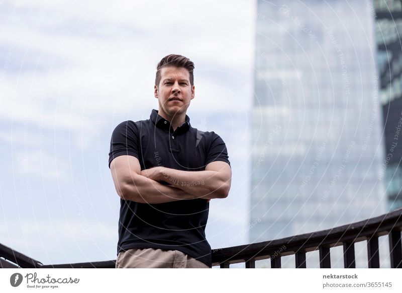 Man with arms folded on sky and building background adult skyscraper caucasian medium shot urban handsome model one person front facing khaki pants balustrade