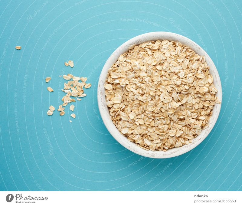 raw oatmeal in a white wooden bowl on a blue background diet organic ingredient dry food breakfast healthy natural cereal vegetarian nutrition closeup grain