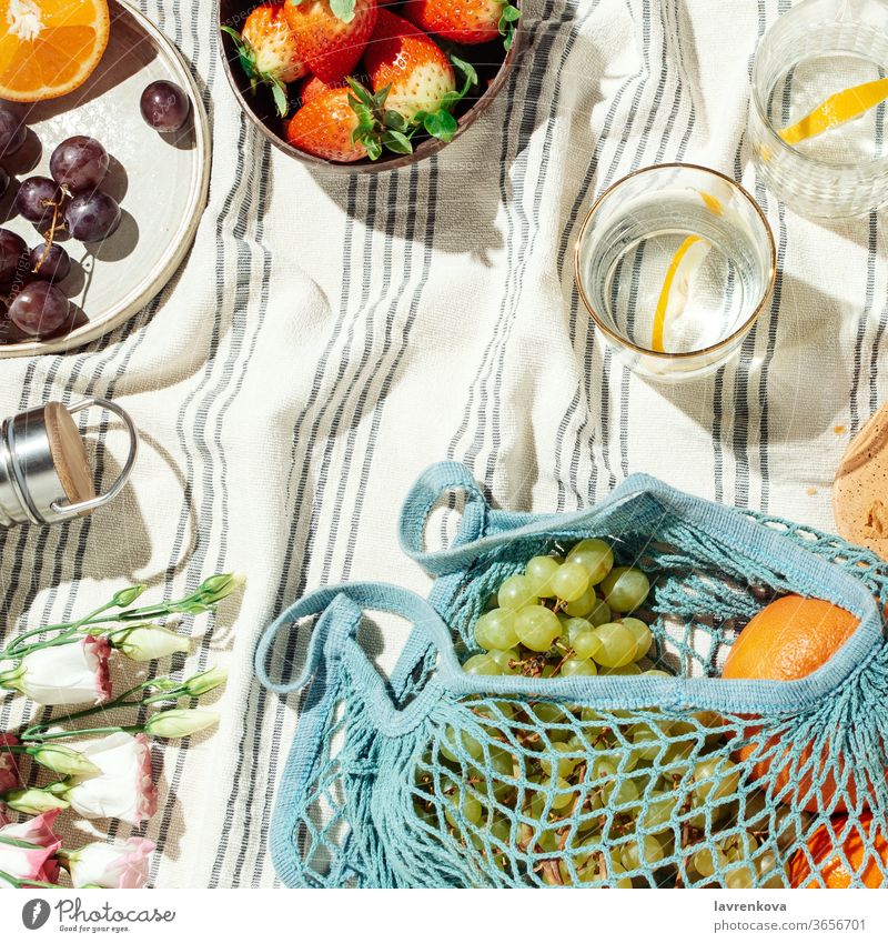 Summer picnic flatlay, fruits, berries and lemon water on striped cotton blanket summer food eating diet fresh glasses citrus seasonal grapes string bag