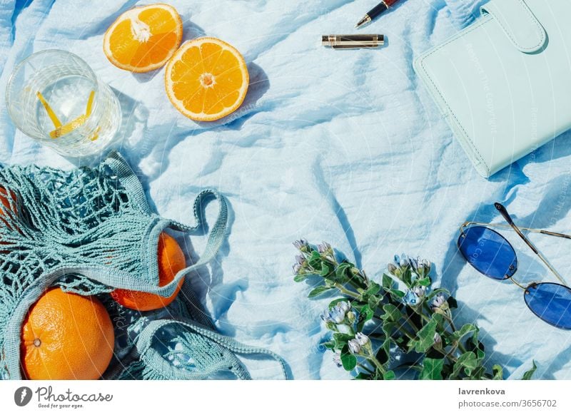 Summer picnic flatlay of fruits, flowers and lemon water on a blue blanket summer glasses citrus seasonal fresh string bag zero waste bouquet spring notebook