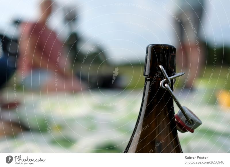 Picnic: Young adults on a picnic blanket with a bottle of beer in the foreground barbecue bbq beer bottle blur cyclist healthy lifestyle man outdoors summer