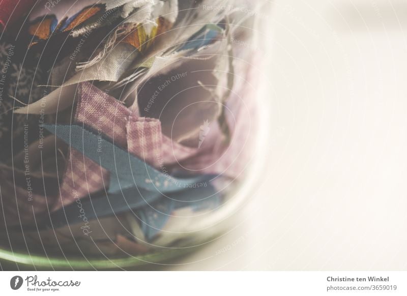 Coloured fabric remnants in a thick-walled glass. Close-up with space for text fabric snippets Cloth Snippets Glass Preserving jar Keep lift Sewing Handcrafts