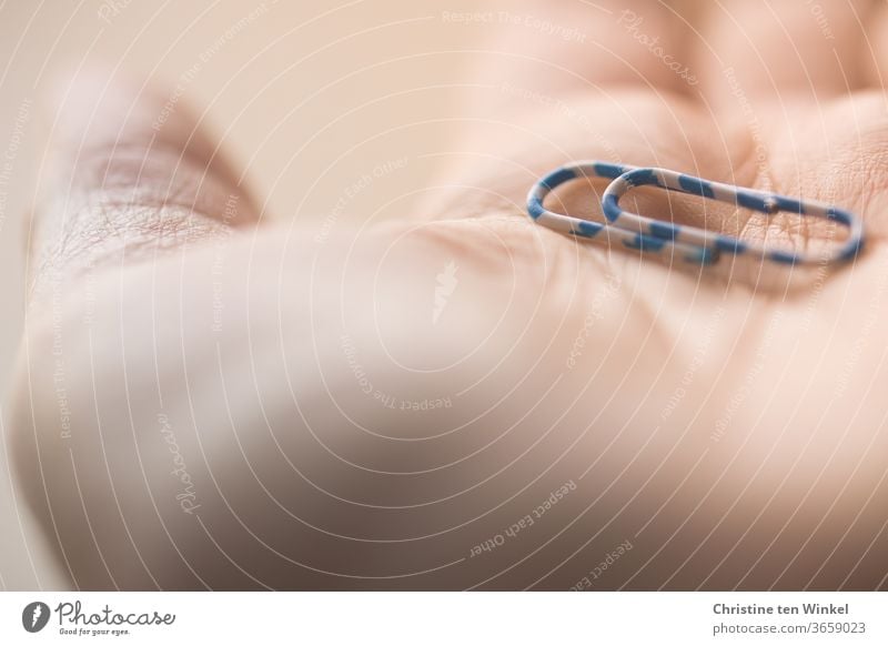 A blue and white striped paper clip lies on an open palm. Close up with shallow depth of field Palm of the hand Thumb Ball of the hand Paper clip Striped