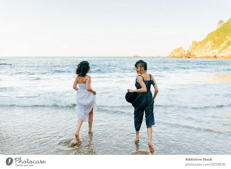 Happy women running on foamy sea near shore beach vacation friend tourism fun barefoot entertain girlfriend harmony ocean together mount partner pleasure hat