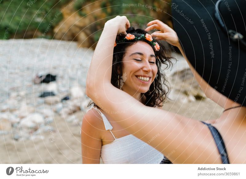 Crop unrecognizable woman putting diadem on head of girlfriend adjust flower beach eyes closed sensual lgbt love lesbian same sex homosexual pond together