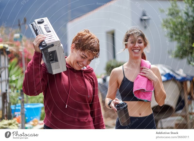 Excited sportswomen with boombox walking in backyard rest country happy excited listen fitness sportswear relax workout together athlete joy strong toothy smile