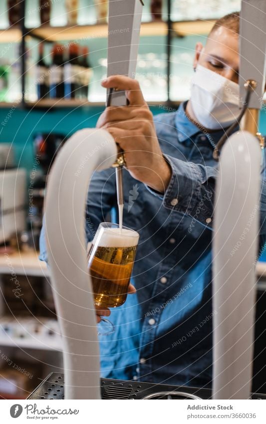 Young man filling glass with beer for client pour tap fresh bartender mask pub draught alcohol drink work male young shirt positive coronavirus covid beverage