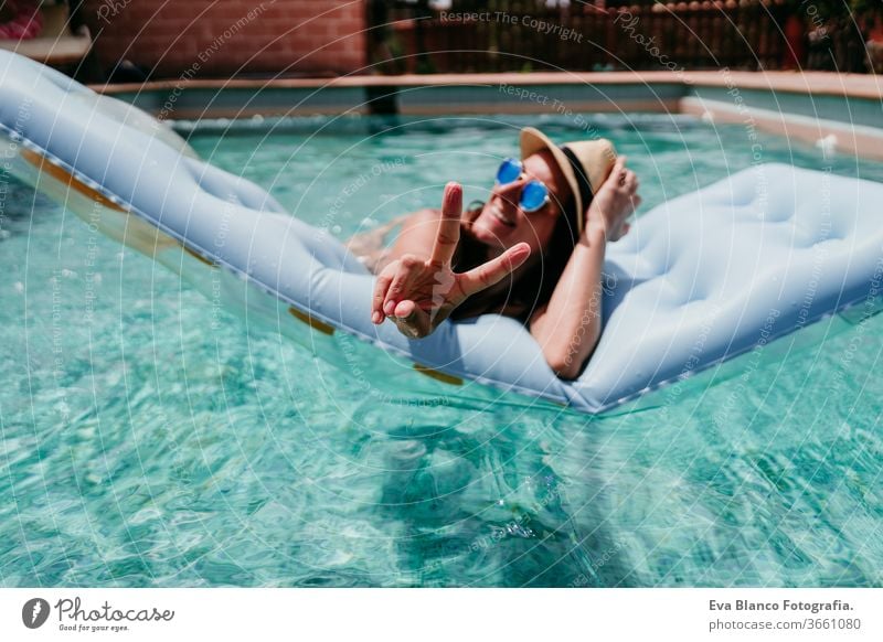 happy woman on inflatable having fun making V sign with fingers. Summer time. v sign smiling swimming pool summer blue water relax hat sexy lifestyle sunglasses