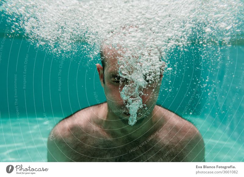 young man diving underwater in a pool making bubbles, summer and fun lifestyle swimming caucasian dive clear health light action wet swimmer blue active float