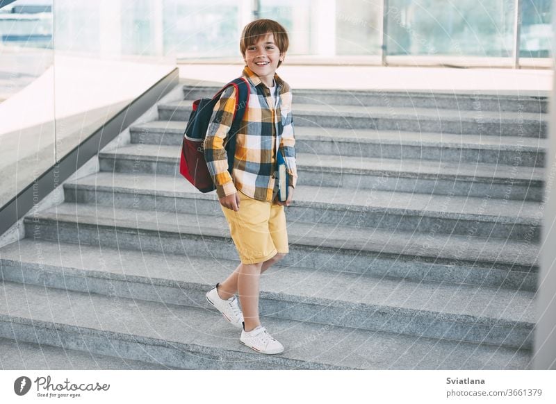 Happy boy with a backpack and a book goes to school. Beginning of the new school year after the summer holidays. Back to school child tablet education small