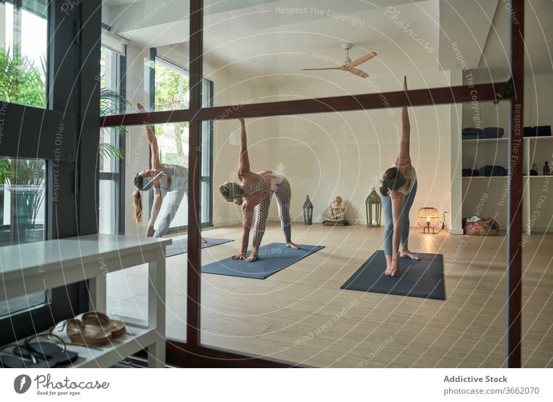 Flexible young female yoga instructors performing extended side angle pose in light studio women practice stretch healthy wellness class Utthita Parsvakonasana