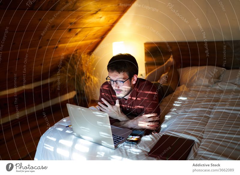 Concentrated male freelancer typing on laptop at home remote man work project entrepreneur using bed lying thoughtful browsing netbook internet device gadget