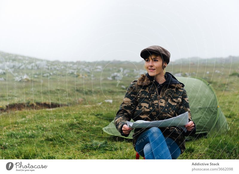 Focused woman with map sitting near camping tent in nature navigate adventure concentrate focus location traveler wanderlust freedom landscape joy casual