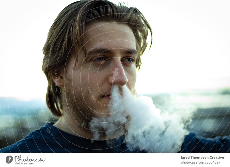 A young man blowing smoke out of his nose. vape youth culture Cigarette Smoking Adults Youth (Young adults) Cigarette smoke smoke trick