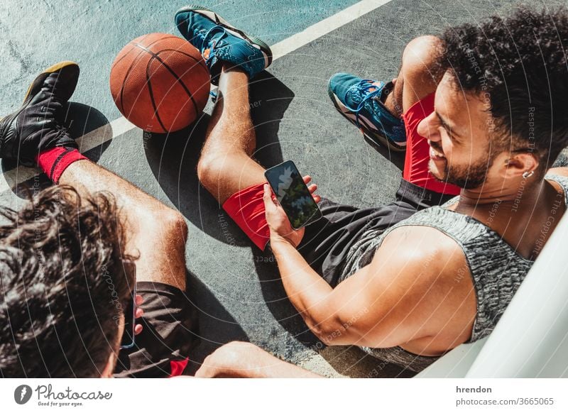 young man rests after the basketball game and uses his smartphone with his friend sport athletic social media competitive smart phone connect cellphone