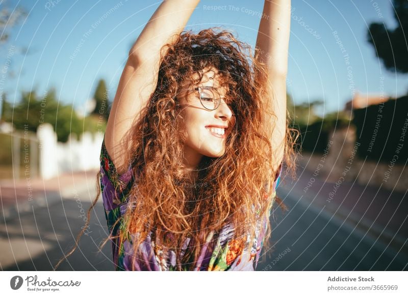 Gorgeous woman with raised arm on asphalt road arm raised toothy smile eyes closed happy lifestyle excited harmony blue sky carefree tree cheerful optimist joy