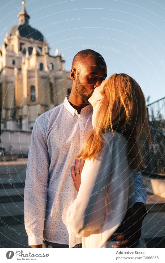 Positive multiethnic couple kissing on street bonding embrace positive candid love content madrid affection gentle casual lifestyle spain sunlight enjoy romance