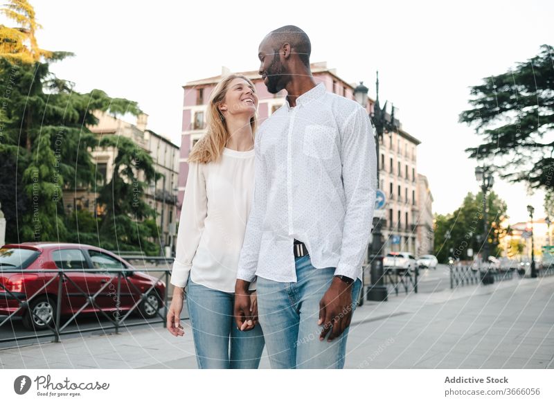 Cheerful diverse couple strolling on street walk urban sidewalk holding hands smile happy cheerful city relationship romance love tender content affection