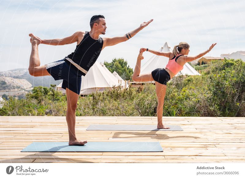 Man and woman doing Lord of Dance pose in open air partner practice yoga camp nature activity balance lord of dance pose flexible harmony health care barefoot